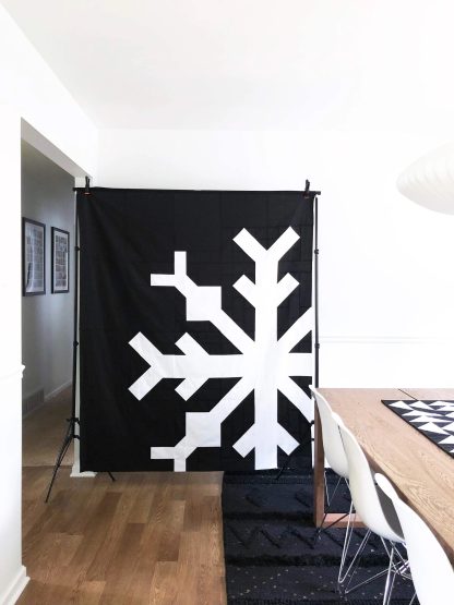 Photo showing the Snowflake Quilt sewing pattern from Modern Handcraft on The Fold Line. A quilt pattern made in quilting cotton fabrics, featuring a snowflake design, there are two ways to assemble this quilt. Use the larger block assembly style for a one-colour or four-colour background or keep it simple with the square and HST scrappy version.