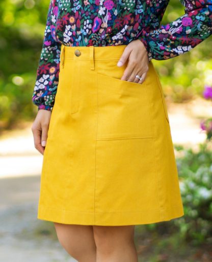 Woman wearing the Taroko Skirt sewing pattern from Itch to Stitch on The Fold Line. A dress pattern made in denim, twill, corduroy, and heavy-weight linen fabrics, featuring an A-line silhouette, contoured waistband, fly front zipper with button closure, back waist darts, belt loops, patch pockets, back patch pockets and above knee length.