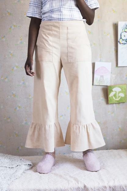Woman wearing the Toril Trousers sewing pattern from Vanessa Hansen on The Fold Line. A trousers pattern made in wool blend suiting, linen/viscose blend, stone-washed linen, chambrays, or general trouser fabrics, featuring a cropped length, hem flounce, side seam invisible zip closure, elasticated waist, and two large patch front pockets.
