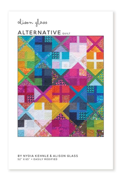 Photo showing the Alternative Quilt sewing pattern from Alison Glass on The Fold Line. A quilt pattern made in quilting cotton fabrics, featuring a design of squares, crosses, and triangles in a rainbow of colours.