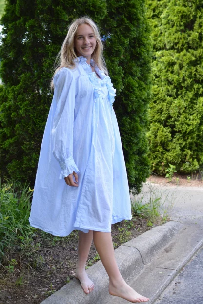 Woman wearing the 224 Beautiful Dreamer sewing pattern from Folkwear on The Fold Line. A nightgown pattern made in cottons, linens, rayons, silks, lawn, dotted Swiss, gauze, voile, muslin, challis, broadcloth or flannel fabrics, featuring a ruffled neckline, below knee length, relaxed fit, back has three deep box pleats, front gathered into ruffled bodice yoke, side seam godets, deep buttoned opening at left front, long puff sleeves, slip-over wristbands with ruffles.