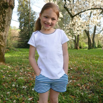 Child wearing the Child/Teen Indie Shorts sewing pattern from Petits D'om on The Fold Line. A shorts pattern made in jersey fabrics, featuring angled front pockets, elasticated waist, and relaxed fit.