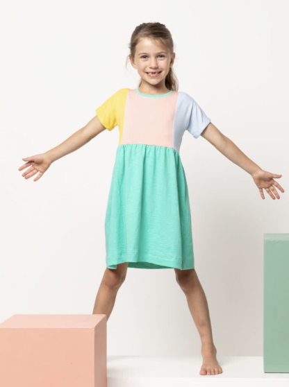 Child wearing the Baby/Child Lacey Dress sewing pattern from Style Arc on The Fold Line. A dress pattern made in jersey, baby wool, rayon or cotton fabrics, featuring a slip-on style, easy fit, extended shoulder line, gathered skirt, in-seam pockets and short sleeves with rolled up hem.