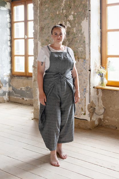 Woman wearing the Pincha Overalls sewing pattern from Ready to Sew on The Fold Line. An overalls/apron combo pattern made in linen or ramie fabrics, featuring a wrap around your hips and waist style, bow tie at front waist, balloon legs, five patch pockets, and front and back darts.