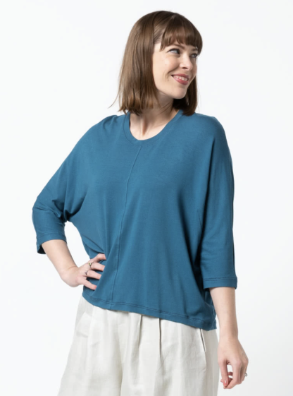 Woman wearing the Rhea Knit Top sewing pattern from Style Arc on The Fold Line. A knit top pattern made in knit jersey, baby wool or French terry fabrics, featuring a relaxed fit, hip-length, crew neck with neckband, bust darts, elbow-length dolman sleeves, high-low hemline, and topstitched front and back seams.