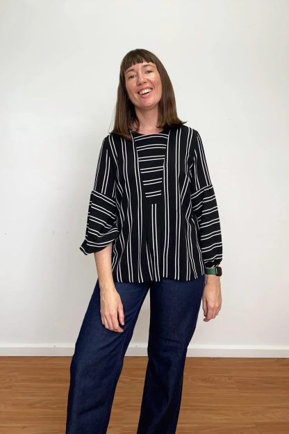 Woman wearing the Sawtell Top sewing pattern from In the Folds on The Fold Line. A top pattern made in linen, linen blends, cotton and lightweight denim fabrics, featuring a hip length, inset placket with pleats, bust darts, yoke, back box pleat, wide hem, round neckline and two-part three-quarter length gathered sleeve with bias cut cuff.