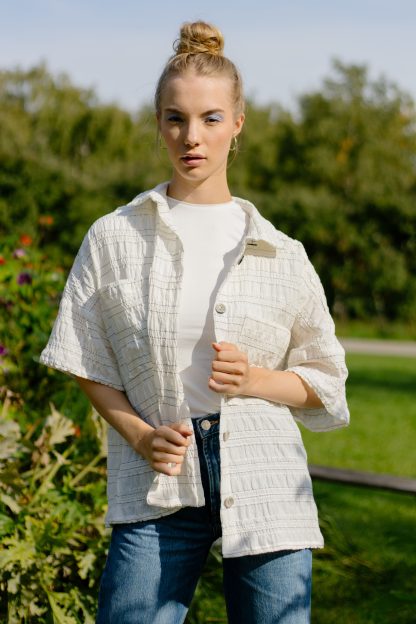 Woman wearing the Gloria Blouse sewing pattern from JULIANA MARTEJEVS on The Fold Line. A blouse pattern made in cotton poplin fabrics, featuring an oversized silhouette, short sleeves, back yoke with pleat, collar, chest patch pocket and front button closure.