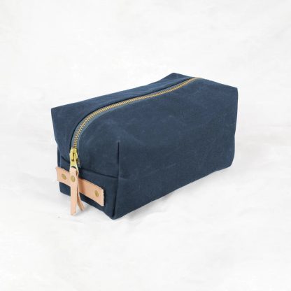 Photo showing the Woodland Dopp Kit sewing pattern from Klum House on The Fold Line. A pouch bag pattern made in canvas, waxed canvas, or denim fabrics, featuring a boxy rectangular silhouette, lined, zip closure, and leather zipper pull.