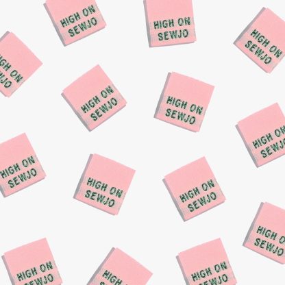 Photo showing 'High on Sew-Jo' Labels from Kylie & The Machine on The Fold Line. A washable, durable, and non-scratchy label. Included are, 6 woven labels with green lettering on a pink background. They are all ready to be sewn into your handmade clothes.