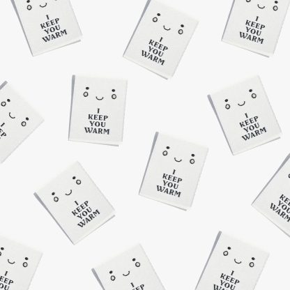 Photo showing 'I Keep You Warm' Labels from Kylie & The Machine on The Fold Line. A washable, durable, and non-scratchy label. Included are, 6 woven labels with black lettering on a white background. They are all ready to be sewn into your handmade clothes.