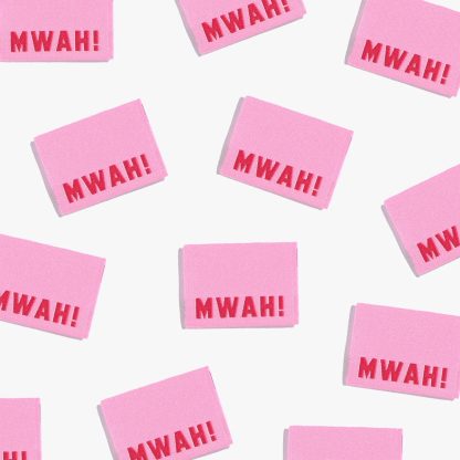 Photo showing 'Mwah!’ Labels from Kylie & The Machine on The Fold Line. A washable, durable, and non-scratchy label. Included are, 6 woven labels with red lettering on a pink background. They are all ready to be sewn into your handmade clothes.