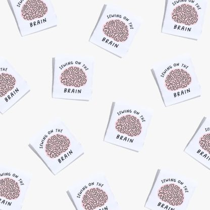 Photo showing 'Sewing on the Brain' Labels from Kylie & The Machine on The Fold Line. A washable, durable, and non-scratchy label. Included are, 6 woven labels showing a brain with black writing on a white background. They are all ready to be sewn into your handmade clothes.