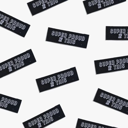 Photo showing 'Super Proud of This' Labels from Kylie & The Machine on The Fold Line. A washable, durable, and non-scratchy label. Included are, 6 woven labels with white writing on a black background. They are all ready to be sewn into your handmade clothes.