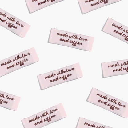 Photo showing 'Made With Love and Coffee' Labels from Kylie & The Machine on The Fold Line. A washable, durable, and non-scratchy label. Included are, 6 woven labels with brown writing on a pale pink background. They are all ready to be sewn into your handmade clothes.