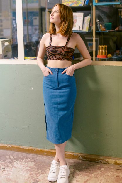 Woman wearing the Frida Skirt sewing pattern from JULIANA MARTEJEVS on The Fold Line. A denim skirt pattern made in stretch denim fabrics, featuring a midi length, straight silhouette, fly front closure, pockets, topstitching, and high slit in the side seam.