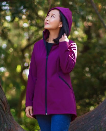 Woman wearing the Andes Jacket sewing pattern from Itch to Stitch on The Fold Line. A jacket pattern made in fleece-backed softshell fabrics, featuring a lined hood, unlined body, princess seams, sleeves with diagonal seam lines, front pockets with exposed zippers, exposed center front zipper, high-low hem and bust cup options.