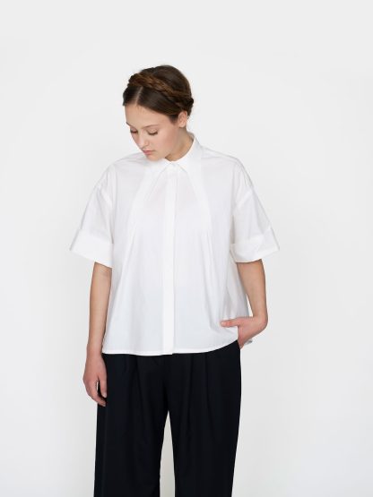 Woman wearing the Front Pleat Shirt sewing pattern from The Assembly Line on The Fold Line. A shirt pattern made in light to medium weight fabrics, featuring a cropped boxy shape, two angled front pleats, back yoke, V-shaped back pleat, short sleeves, and hidden button placket.
