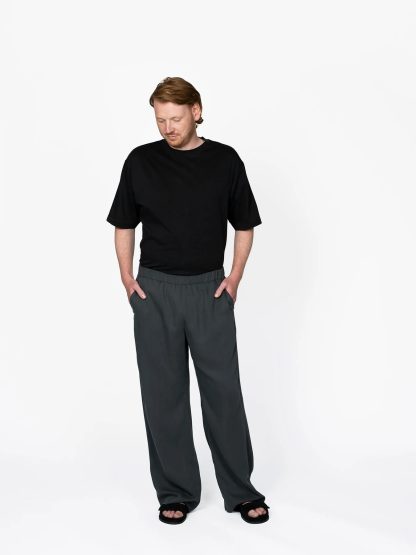 Man wearing the Men's Pull-on Trousers sewing pattern from The Assembly Line on The Fold Line. A trouser pattern made in cotton, linen, viscose, wool, lightweight twill fabrics, featuring an elastic waist, wide legs, slant pockets and side stripes.