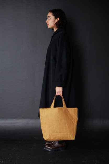 Woman holding the Sturdy Tote sewing pattern from Merchant & Mills on The Fold Line. A bag pattern made in oilskin, dry oilskin, cotton canvas or drill, and denim fabrics, featuring a lining, inner pockets, and turned through handles.