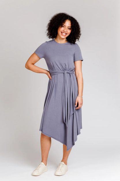 Woman wearing the Floreat Dress and Top sewing pattern from Megan Nielsen on The Fold Line. A dress pattern made in cotton, linen, chambray, rayon, or silk fabrics, featuring an asymmetrical hem, in-seam pockets, short sleeves, round neck, invisible back zip closure and self-fabric waist tie.