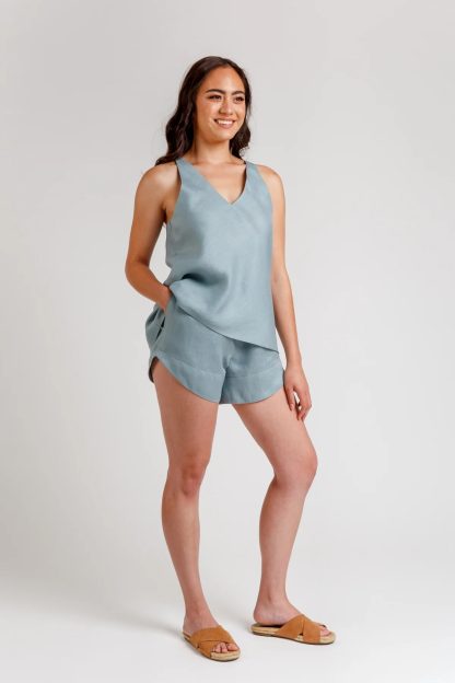 Woman wearing the Reef Camisole and Shorts Set sewing pattern from Megan Nielsen on The Fold Line. A camisole and shorts pattern made in shirting, linen, rayon, tencel, lawn, light chambray, charmeuse and crepe de chine fabrics, featuring a bias-cut camisole with V-neck, crossover back yoke, sleeveless. Shorts have elastic waist, pockets, curved hemline.
