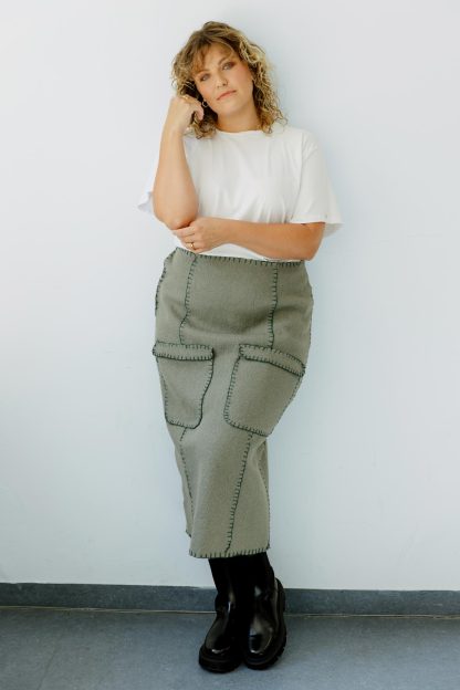 Woman wearing the Molly Skirt sewing pattern from JULIANA MARTEJEVS on The Fold Line. A blanket stitch hand sewn skirt pattern made in wool loden fabrics, featuring a midi length, back slit, front patch pockets and snap side closure.