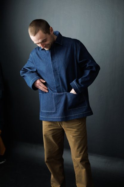Man wearing the Unisex Ludlow Top sewing pattern from Merchant & Mills on The Fold Line. A top pattern made in cotton canvas and twill, dry oilskin, oilskin, denim and corduroy fabrics, featuring a pull-over smock style, integrated pockets, collar, concealed half button placket, full length sleeves, and relaxed fit.