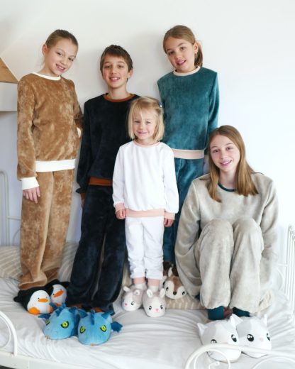 Children wearing the Child/Teen Pilou Pyjamas sewing pattern from Petits D'om on The Fold Line. A pyjamas pattern made in sweatshirt or jersey fabrics, featuring a bottom with a straight cut, elasticated waist, and ribbed hem bands. Top is relaxed fitting, round neck, long sleeves and neckline, hem and sleeves are finished with ribbing.