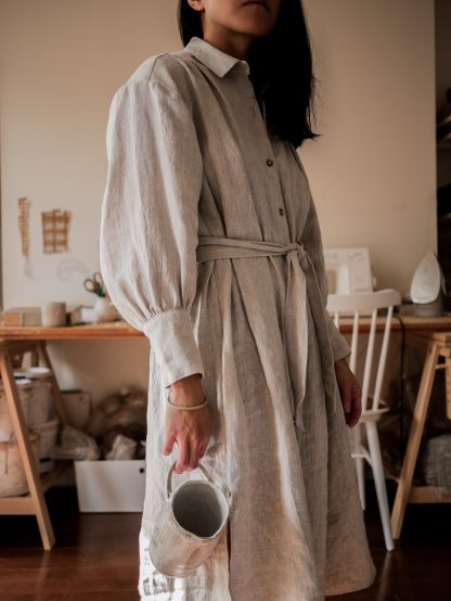 Woman wearing the Terra Dress sewing pattern from Vivian Shao Chen on The Fold Line. A shirt dress pattern made in cotton or linen fabric, featuring a relaxed fit, front button placket, collar stand and fall, slightly dropped sleeves gathered into cuffs, and a self fabric belt.