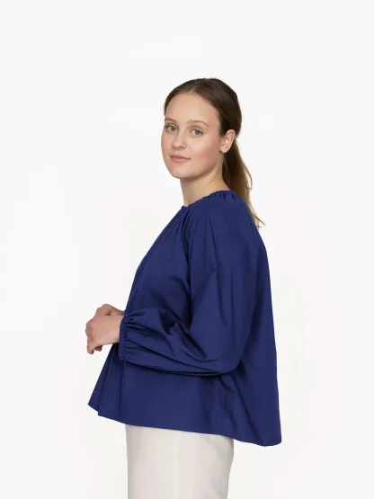 Woman wearing the Billow Blouse sewing pattern from The Assembly Line on The Fold Line. A blouse pattern made in light to medium weight fabric, featuring a voluminous shape, round neckline gathered with elastic, and raglan sleeves with elastic cuffs.