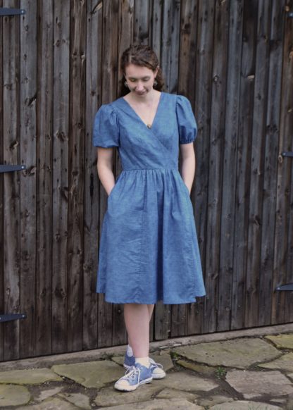 Woman wearing the Blossom Wrap Dress sewing pattern from Stitched in Wonderland on The Fold Line. A dress pattern made in cotton, viscose, or linen fabric, featuring a lined bodice, short gathered puff sleeves, a gathered skirt, and pockets.