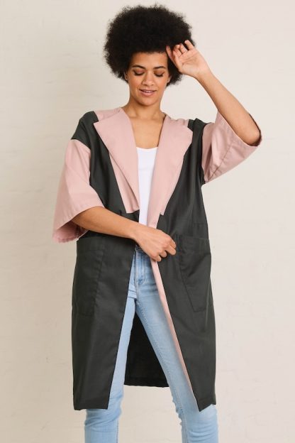 Woman wearing the Inez Summer Jacket sewing pattern from Atelier Jupe on The Fold Line. A jacket pattern made in viscose, tencel, cotton, linen, or polyester fabric, featuring a relaxed knee-length silhouette, wide half-length sleeves, large topstitched front pockets, and seamlines for colour blocking.