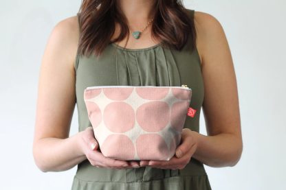 Woman holding the Lily Pouches Set sewing pattern from Pattern Scout on The Fold Line. A bag pattern made in quilting cotton, linen, canvas, twill, bull denim, upholstery fabric, or waxed canvas, featuring gussets at the base to create a flat bottom, ideal for toiletries and makeup.