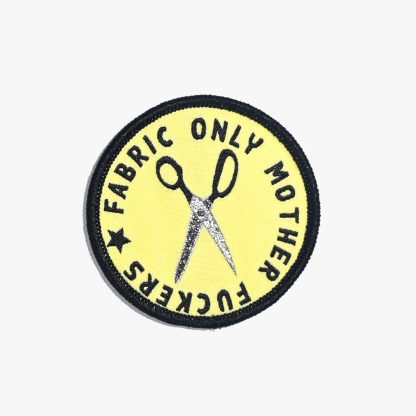 Photo of the ‘Fabric Only Mother Fuckers’ iron-on patch from Kylie & The Machine on The Fold Line. A round patch featuring scissors and black text on a yellow background with a black border ready to be attached to your handmade garment or bag.