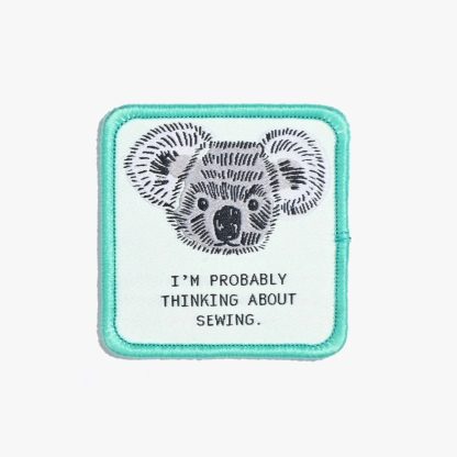 Photo of the ‘I’m Probably Thinking About Sewing’ iron-on patch from Kylie & The Machine on The Fold Line. A square patch featuring a koala with a mint green background and border ready to be attached to your handmade garment or bag.