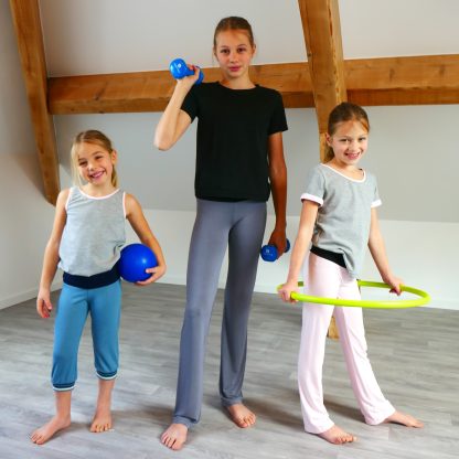 Children wearing the Child/Teen Zen Pants sewing pattern from Petits D’om on The Fold Line. A pants pattern made in cotton/elastane jersey fabric, featuring long and cropped lengths, a wide waistband, snug fit around the hips, and straight legs.