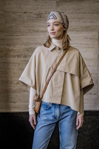 Woman wearing the Delma Cape sewing pattern from Fibre Mood on The Fold Line. A cape pattern made in wool or cotton fabrics, featuring a pleat at the back, side seam closures, hidden button fastening, front storm flap, and options for a collar or hood.