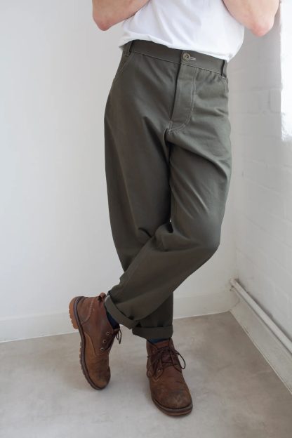 Man wearing the Men's Worker Trousers sewing pattern from The Modern Sewing Co. on The Fold Line. A trousers pattern made in medium/heavy denim, medium/heavy twill, canvas, corduroy/needlecord, wool suiting, or sturdy linen fabric, featuring a slight balloon in the leg, taper towards the ankle, concealed button or zip fly finished with binding, front and back pockets, and a waistband with belt loops.