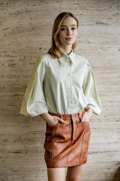 Woman wearing the Odyna Blouse sewing pattern from Fibre Mood on The Fold Line. A shirt pattern made in poplin, textured cotton, double gauze, chambray, lyocell, or crepe fabric, featuring a loose fit, button front, A-line pleated sleeve or long straight sleeve, and pointed collar.