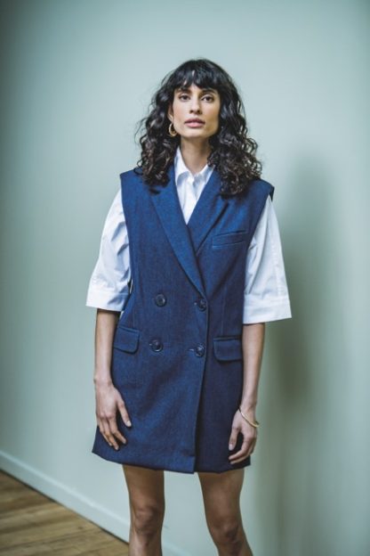 Woman wearing the Perla Dress sewing pattern from Fibre Mood on The Fold Line. A sleeveless dress pattern made in cotton twill, polycotton, denim, linen or woollen fabrics such as tweed, flannel and fine virgin wool, featuring an oversized fit and blazer-like styling with a double-breasted front, welt pockets, and lining.