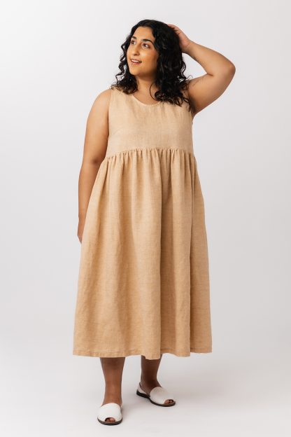 Woman wearing the Taimi Dress sewing pattern from Named on The Fold Line. A sleeveless dress pattern made in cotton or linen fabric, featuring a round neckline, curved waist seam, voluminous gathers, and side pockets.