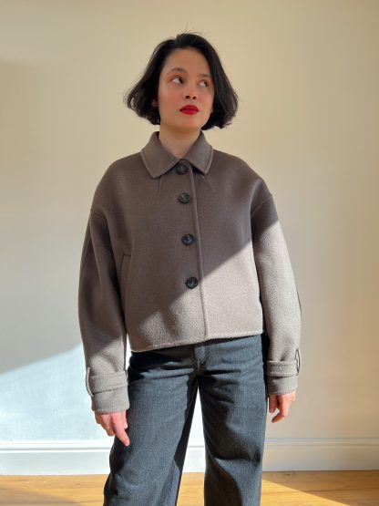 Woman wearing the Kaia Coat sewing pattern from Bella Loves Patterns on The Fold Line. A short coat pattern made in double faced coating fabric, featuring an oversized silhouette, dropped shoulder line, bal collar with a collar stand, button closure, welt pockets, sleeves with a wrist strap, and high hip length.
